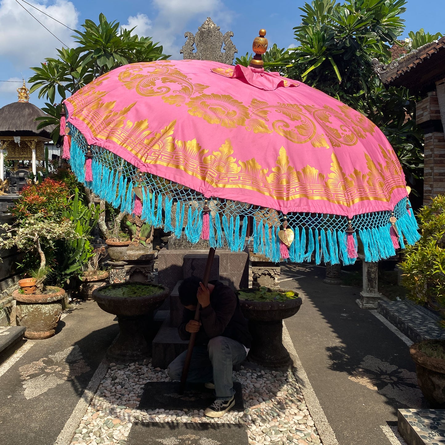 Handmade Balinese umbrella in pink with golden motifs and blue fringes, perfect for decoration and ceremonies.