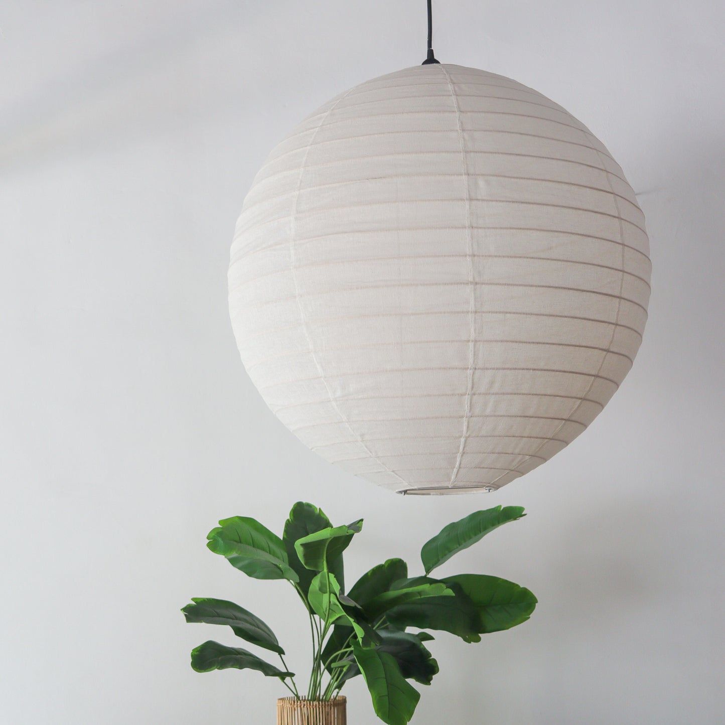 Off white round linen lantern chandelier hanging above a green plant, handcrafted in Bali.