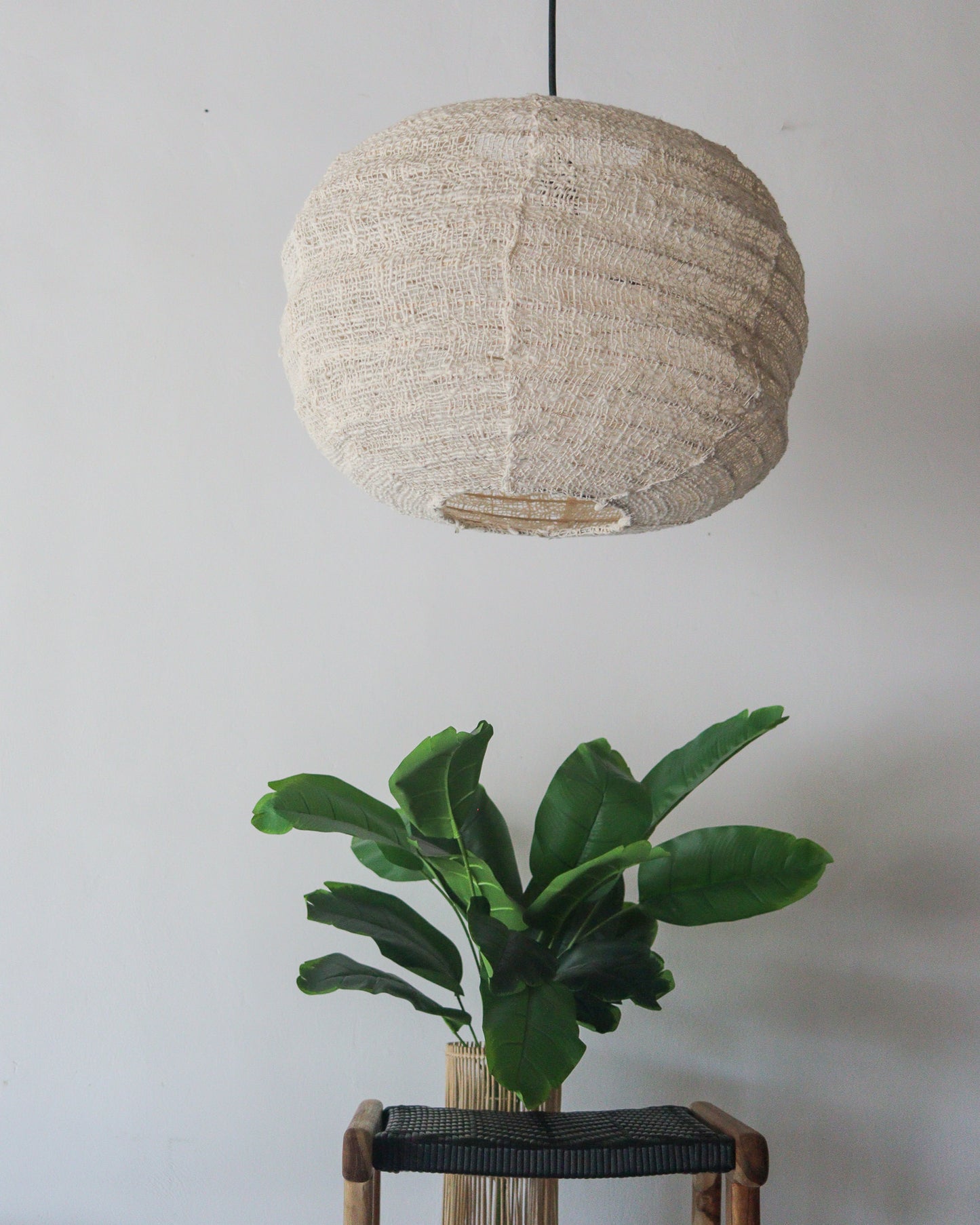 Handmade cotton chandelier lantern with pumpkin shape, suspended above a green plant in a stylish interior.