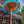 Balinese decorative umbrella with blue fringe and ornate patterns beside a brick wall outdoors