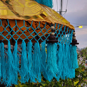 Balinese decorative parasol with golden patterned fabric and blue tassels outdoors