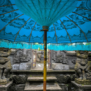 Balinese stone temple entrance with blue decorative umbrella and intricate carvings