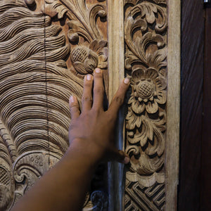 Hand touching hand-carved Balinese wooden wall panel with intricate floral design