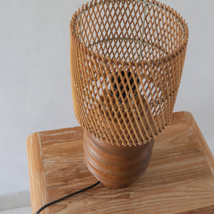 Handcrafted Bali wooden table lamp with woven rattan shade on rustic wood surface