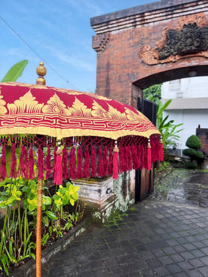 Balinese maroon umbrella with gold motif and tassels in front of stone gate