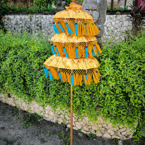 Balinese triple-tiered yellow parasol with blue tassels in a tropical garden setting