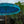 Handcrafted Balinese garden parasol with blue fringe, tropical plants and stone statue background