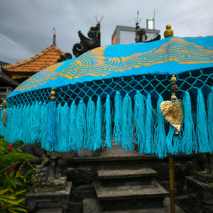 Balinese blue parasol with gold accents and decorative tosca fringe outdoors