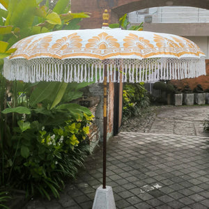 Balinese decorative parasol with yellow classic motif and white fringe, outdoor garden setting