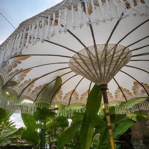 Balinese decorative umbrella with gold patterns and tassels in a tropical garden setting
