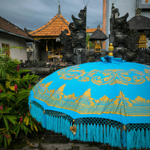 Balinese blue and gold decorative umbrella with tassels near traditional temple garden