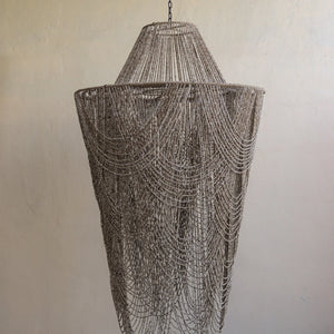 Handmade beige bead chandelier with cascading strands, hanging against a neutral wall