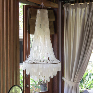 Handmade seashell chandelier hanging in a sunlit room with wooden accents and curtains.
