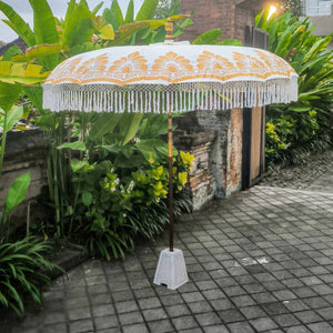 Large Balinese umbrella with gold patterns and fringe, set in tropical garden patio