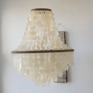 Natural capiz shell chandelier with round shells in a tiered hanging design against a white wall.