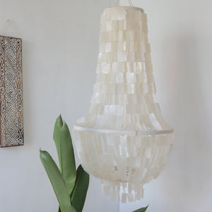 Large capiz shell chandelier hanging in a minimalist room with green plant and wall art.