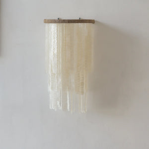 Handmade capiz shell wall hanging with cascading white discs on a neutral wall.