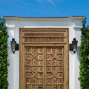 Hand-carved vintage Balinese wooden door with ornate detailing and iron studs outdoors