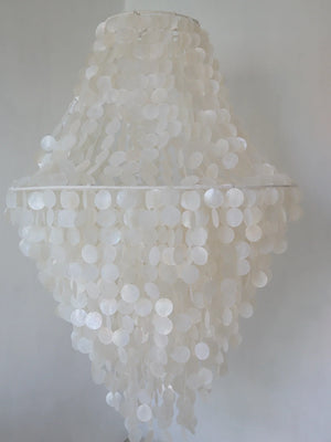 Handmade seashell chandelier with cascading white shell discs against a neutral wall