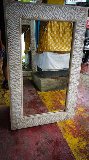 Hand-carved Balinese mirror with intricate geometric border on rustic floor