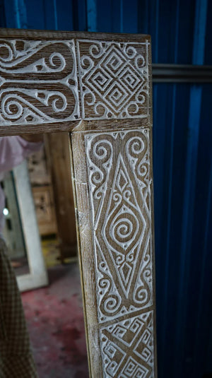 Hand-carved wooden mirror frame with intricate Balinese patterns in rustic white finish