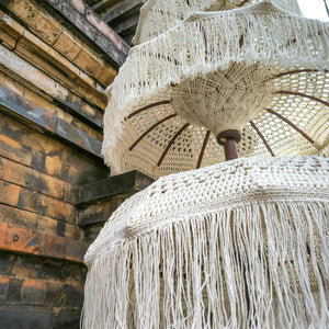 Handmade Balinese decorative umbrella with macrame fringe against stone wall