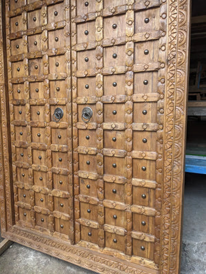 Hand-carved double wooden door with intricate panel design and decorative metal handles