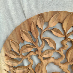 Hand-carved wood wall art with intricate leaf and branch design on a light fabric background