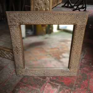 Hand-carved Balinese wood mirror with intricate geometric patterns on a rustic floor
