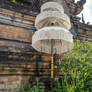 Handcrafted Balinese parasol with white fringe by a traditional stone wall and greenery
