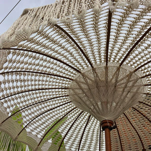 Hand-knitted macrame Balinese umbrella with intricate patterns and fringe outdoors.