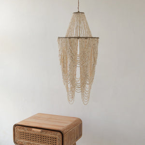Handmade seashell chandelier ceiling light above carved wooden nightstand in minimalist room