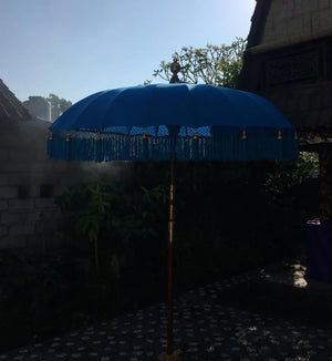 Blue Balinese decorative umbrella with gold tassels in a tropical outdoor setting