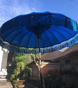 Blue Balinese parasol with tassels in tropical garden courtyard, traditional decor