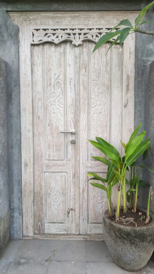 Hand-carved Balinese wooden door with floral patterns, potted plant beside entrance