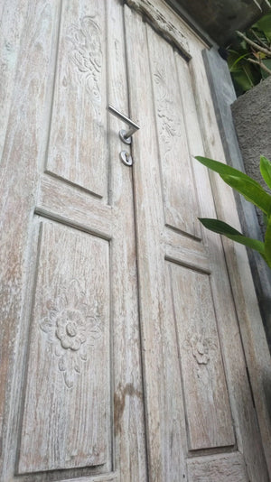 Hand-carved Balinese wooden door with floral engravings and rustic finish outdoors
