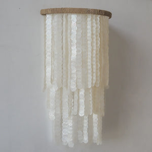 Handmade white seashell chandelier with cascading strands against a plain wall