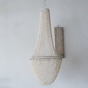 Handmade seashell chandelier with intricate beading, hanging on a white wall.
