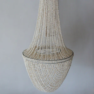 Handmade Balinese seashell chandelier with cascading white shell strands against a gray wall