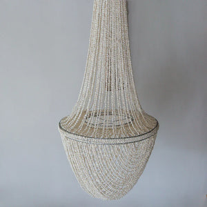 Handmade Balinese seashell chandelier with cascading white shell strands against a gray wall