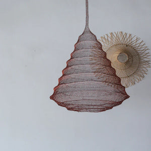 Handmade woven pendant light with a natural, wavy design hanging against a plain wall.