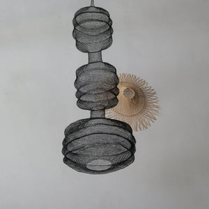 Handmade black wire pendant lamp beside a natural woven rattan wall sconce on white wall