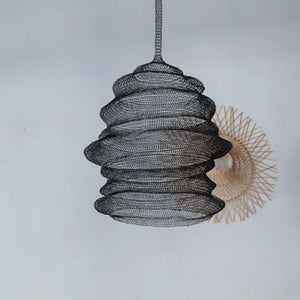 Handcrafted black wire mesh pendant lamp with modern sculptural design against light wall.