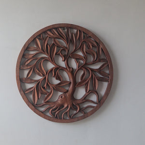 Hand-carved wooden tree of life wall art with intricate roots and leaves on a plain wall