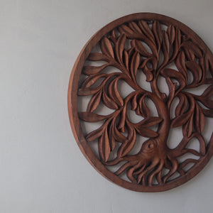 Hand-carved Balinese wood wall art featuring a tree of life design on a plain wall.