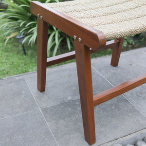 Handmade wooden bench with woven rattan seat on outdoor stone patio, garden background