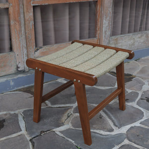 Handcrafted wooden and rattan stool with woven seat on stone patio near rustic door
