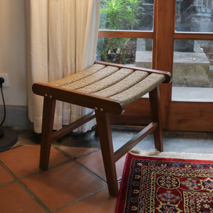 Handcrafted wooden stool with woven seat in a cozy room, near window and patterned rug.