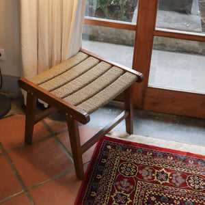 Handmade wooden stool with woven seat in a cozy living room by a glass door