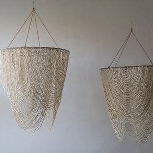 Handmade Balinese seashell chandeliers with draped natural shell strands on a plain wall